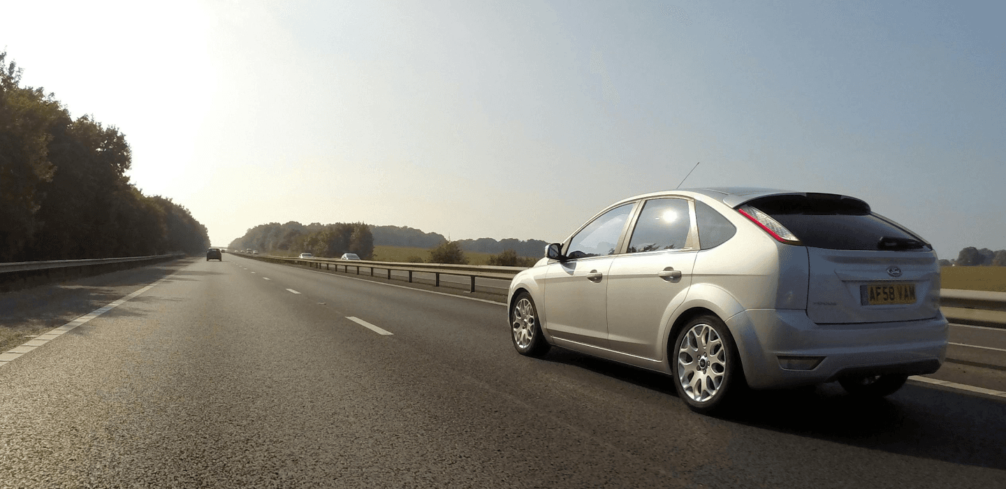 Srebrny Ford Focus jadący autostradą w słoneczny dzień – opony letnie o niskich oporach toczenia.