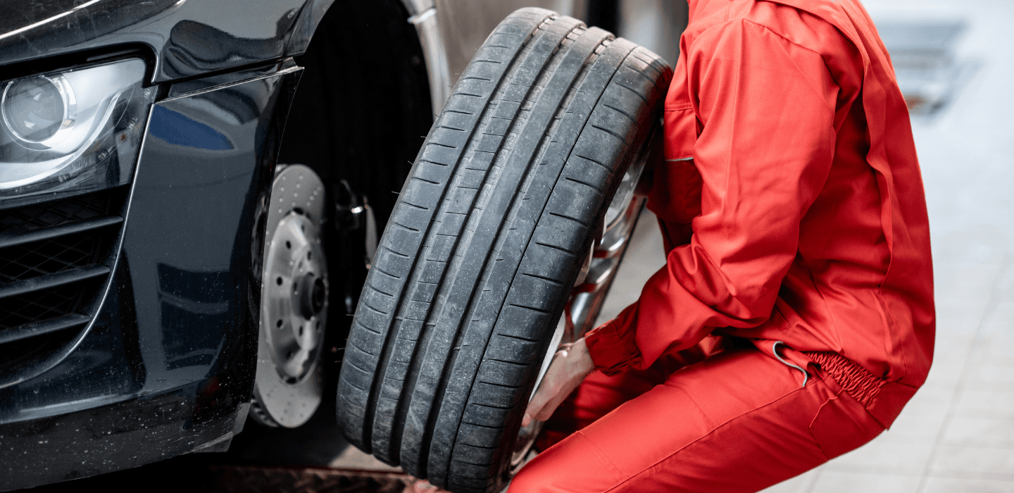 Mechanik w czerwonym kombinezonie zdejmujący koło z samochodu sportowego – serwis hamulcowy i wymiana opon.