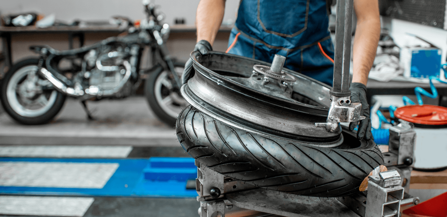 Mechanik w warsztacie montujący nową oponę na felgę motocyklową przy użyciu profesjonalnej montażownicy.