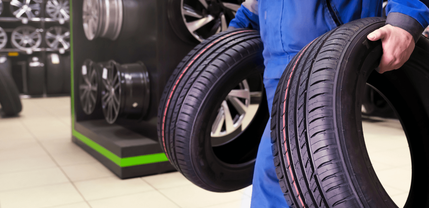 Pracownik serwisu opon przenoszący dwie nowe opony osobowe w profesjonalnym magazynie ogumienia i felg.