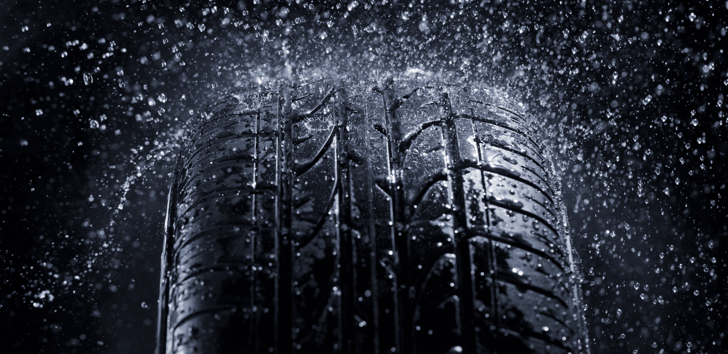 Zbliżenie na bieżnik opony osobowej w rzęsistym deszczu – test przyczepności i bezpieczeństwa opon na mokrej nawierzchni.