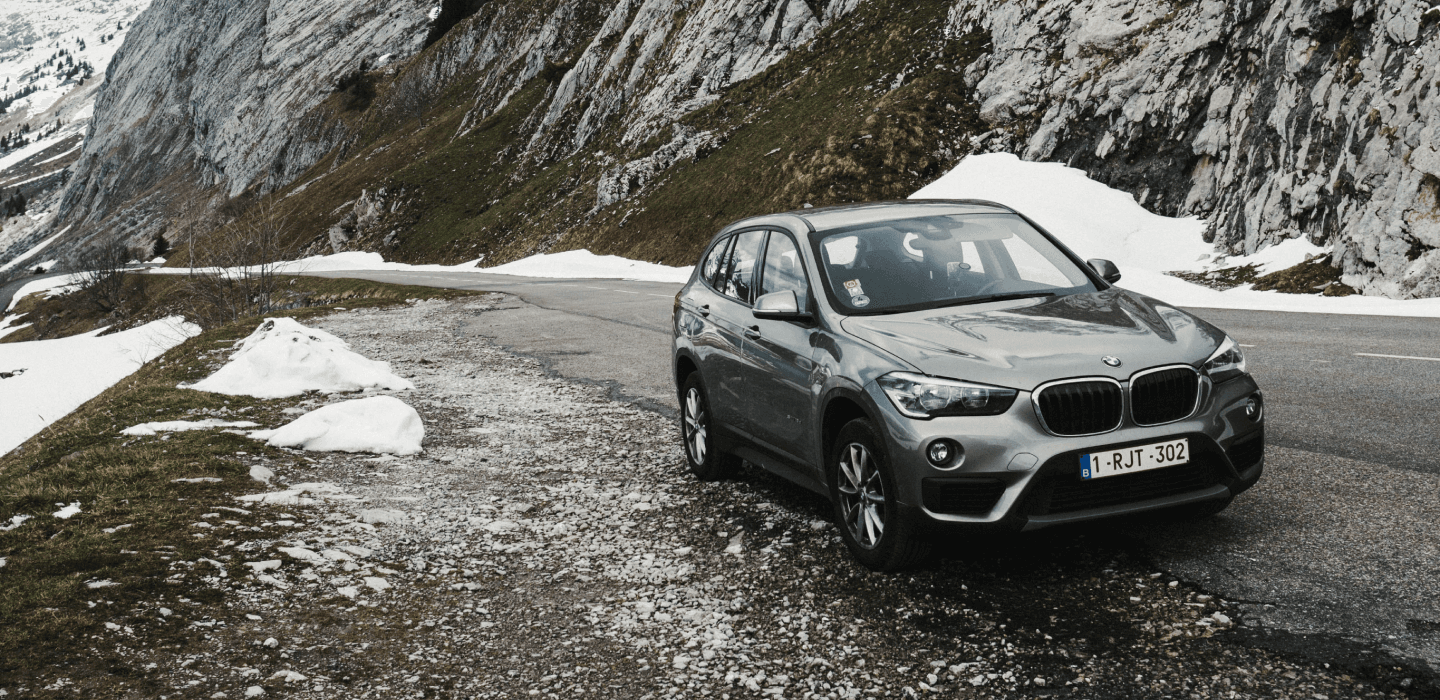 Szary SUV BMW X1 na górskiej drodze z resztkami śniegu – opony zimowe w warunkach alpejskich.